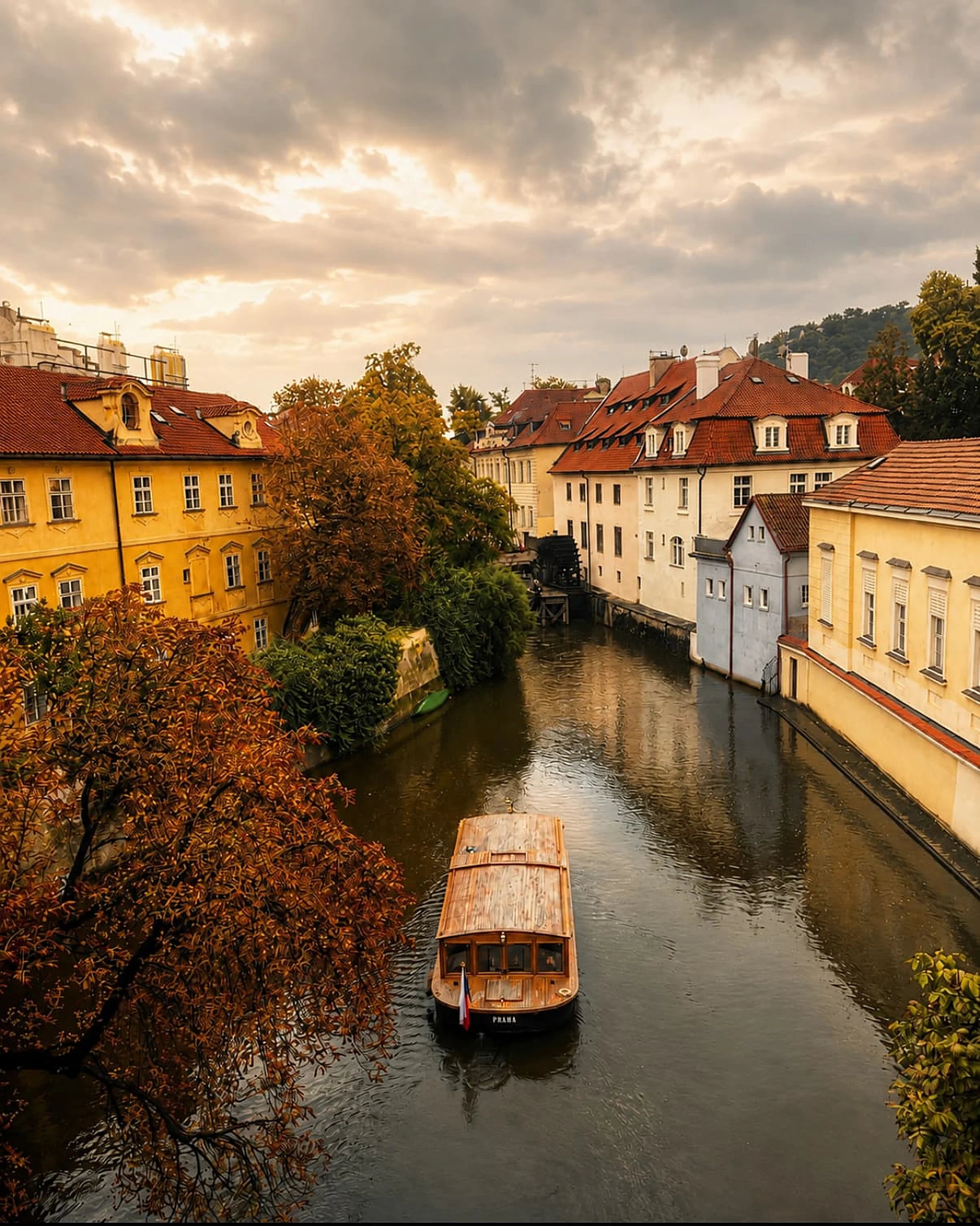 A small boat on a still Prague canal beneath pale buildings and a low bridge