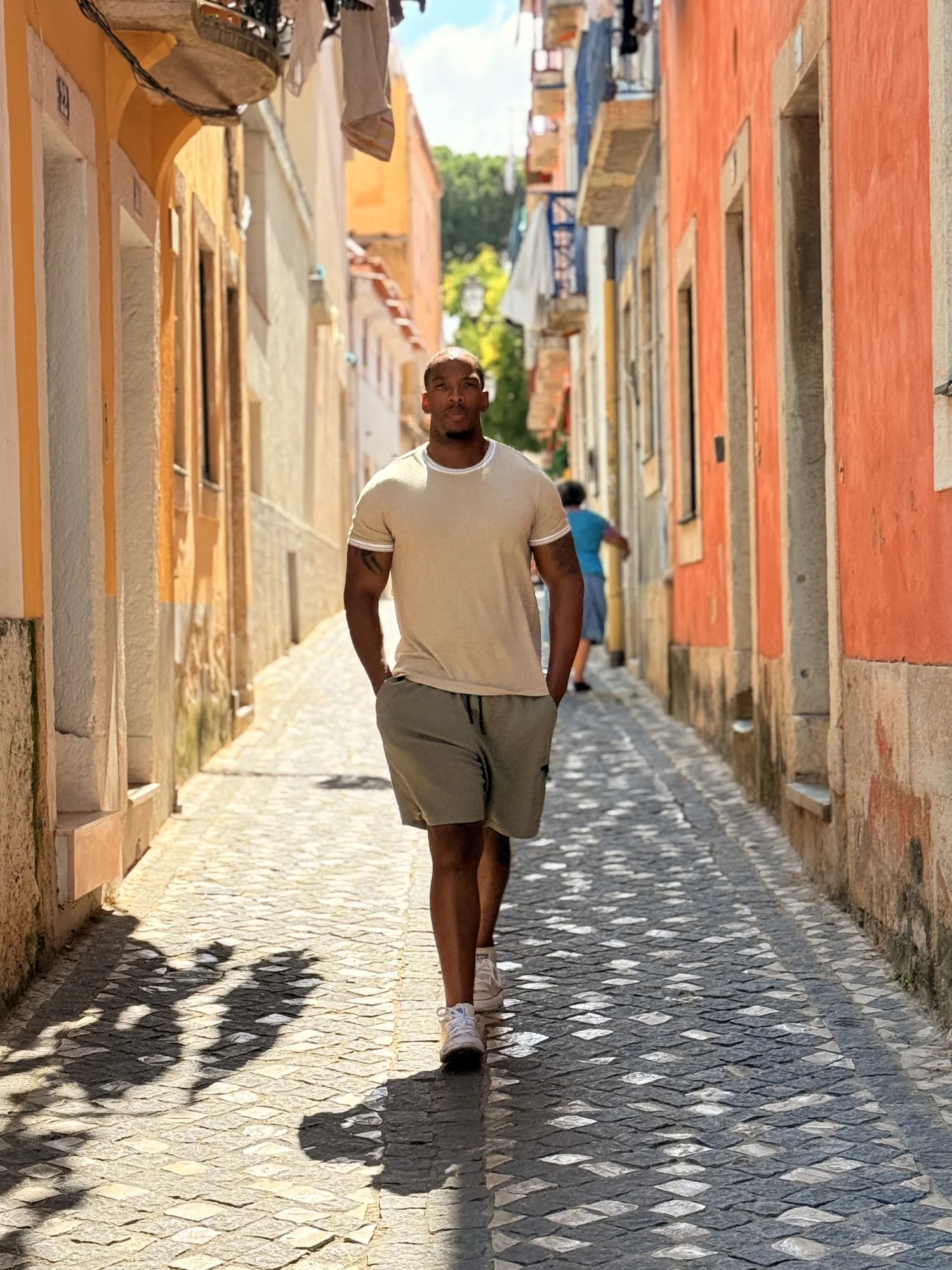 Jonathan walking through a sunlit street in Portugal, looking towards the buildings ahead